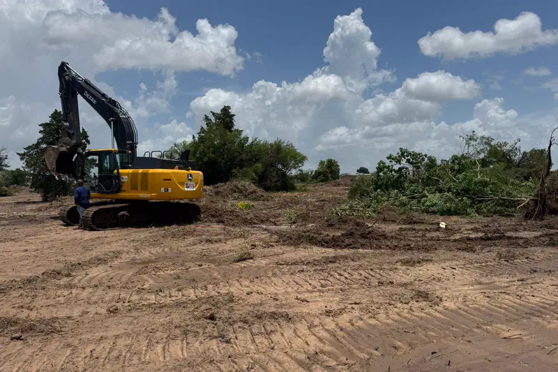 A tracked excavator beside windrowed brush on a cleared site