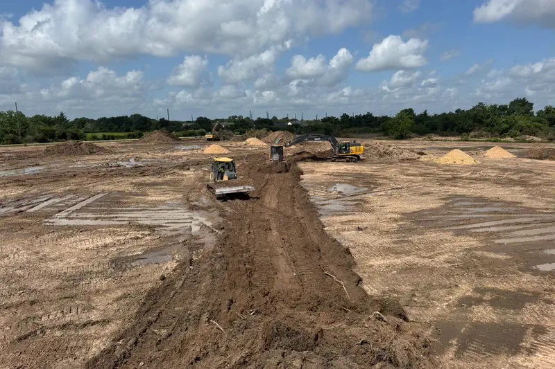 A dozer and two excavators cutting a drainage line across a wet site